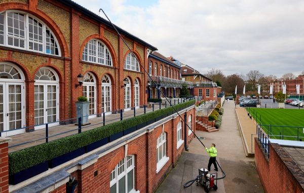 Tagrenderensning med sugestang fra jorden ved en murstensbygning.